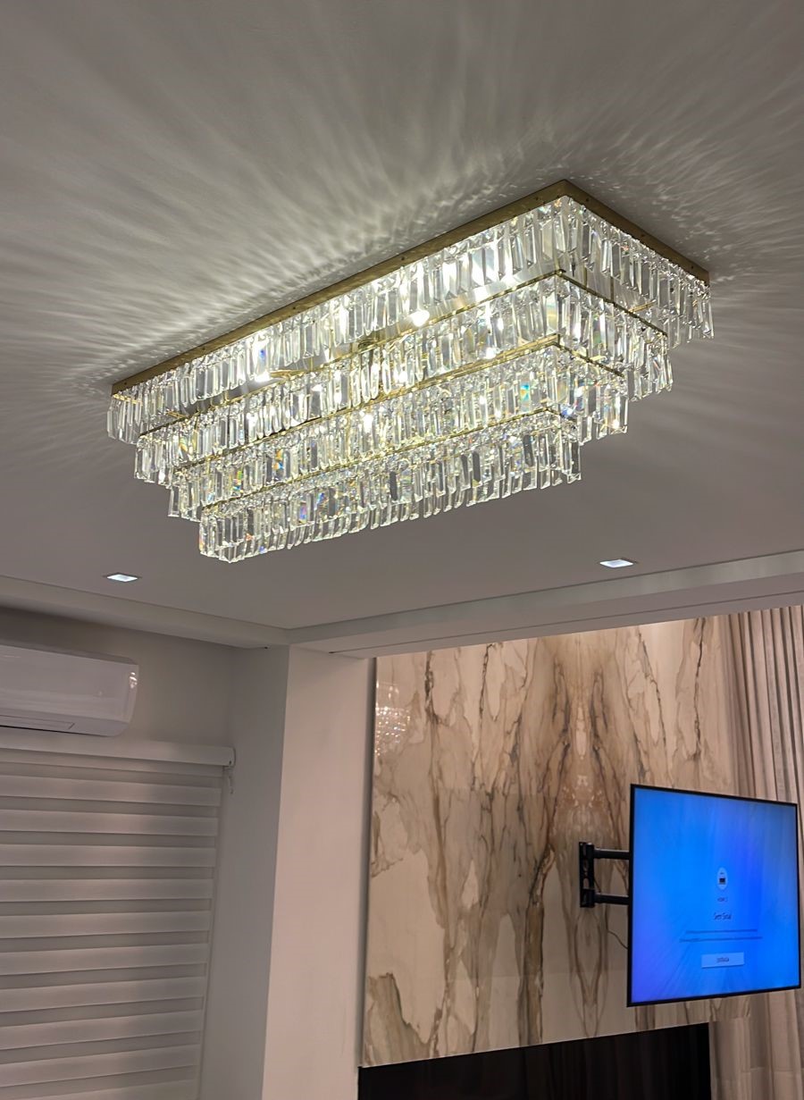 Lustre de Cristal Maia 60x20 Retangular iluminando uma elegante sala de jantar com mesa e cadeiras estofadas. Lustres Gênesis loja online de Lustres e Iluminação Decorativa. 